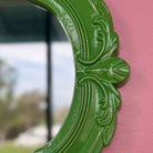 Decorative green mirror with intricate designs on a pink background