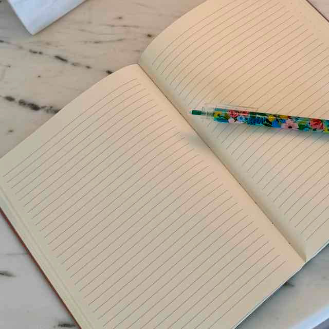 Open notebook with lined pages and a colorful pen on a wooden surface