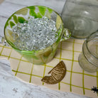 Clear glass bowl with green rim filled with clear stones on a checkered surface.