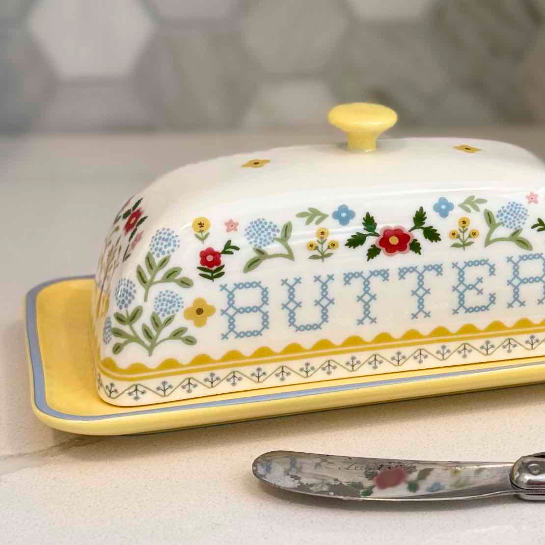 Decorative butter dish with floral patterns and the word 'BUTTER' on a neutral background