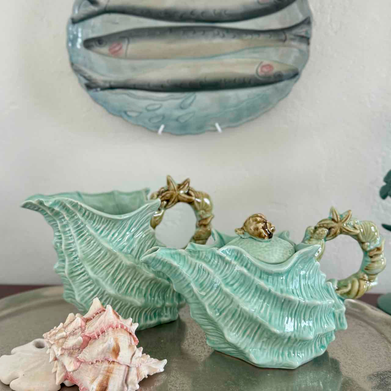 Decorative shell-shaped teapot and pitcher with a seashell on a neutral background