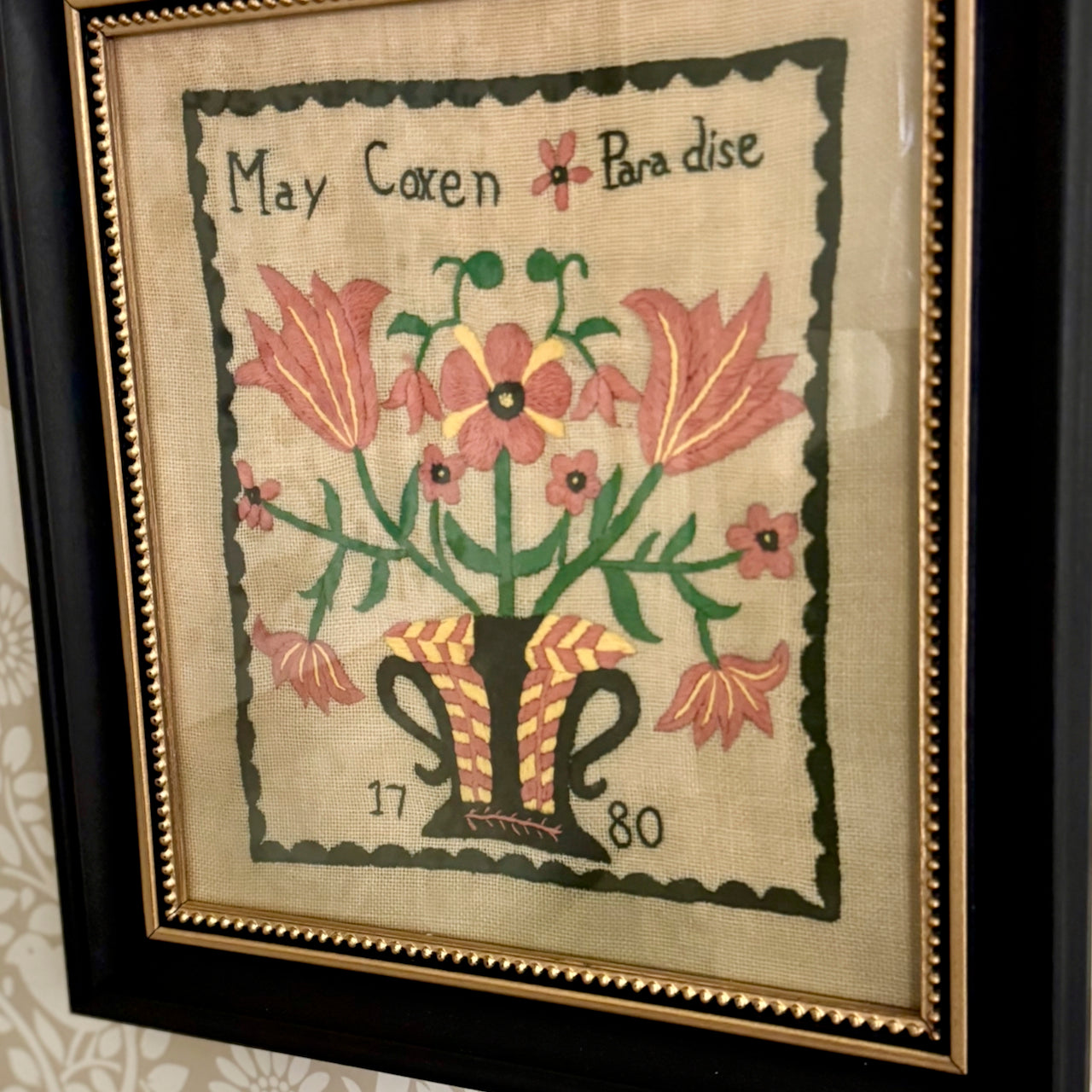 Framed embroidered artwork with floral design and text 'May Coven Paradise' on a textured fabric background.