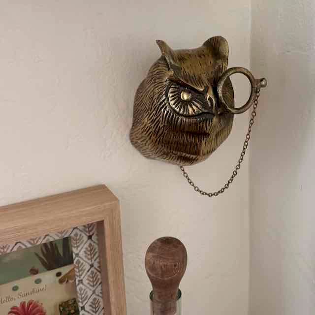 Decorative wall-mounted owl with a chain on a light-colored wall.