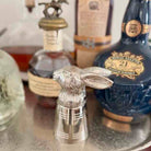 Silver rabbit-shaped decanter stopper in front of whisky bottles