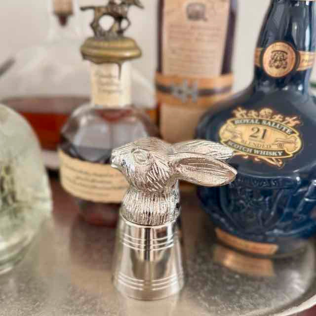 Silver rabbit-shaped decanter stopper in front of whisky bottles