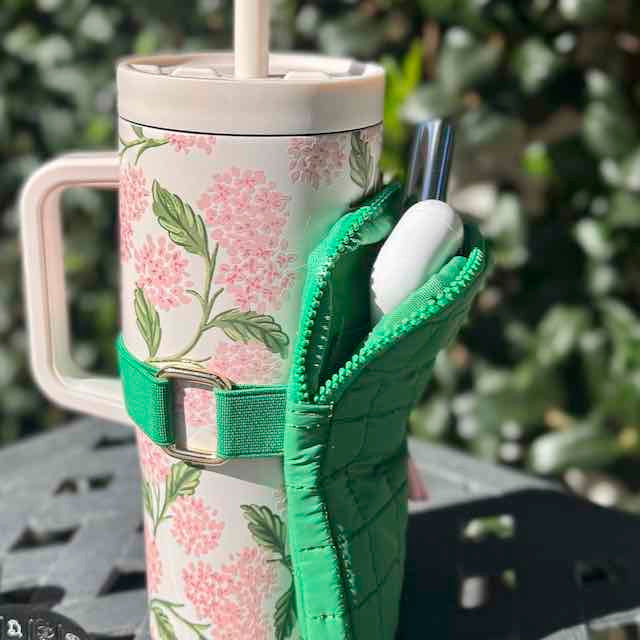 Floral-patterned tumbler with a green holder on a blurred outdoor background