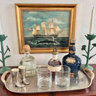 Tray with bottles and glasses in front of a framed painting of a ship.
