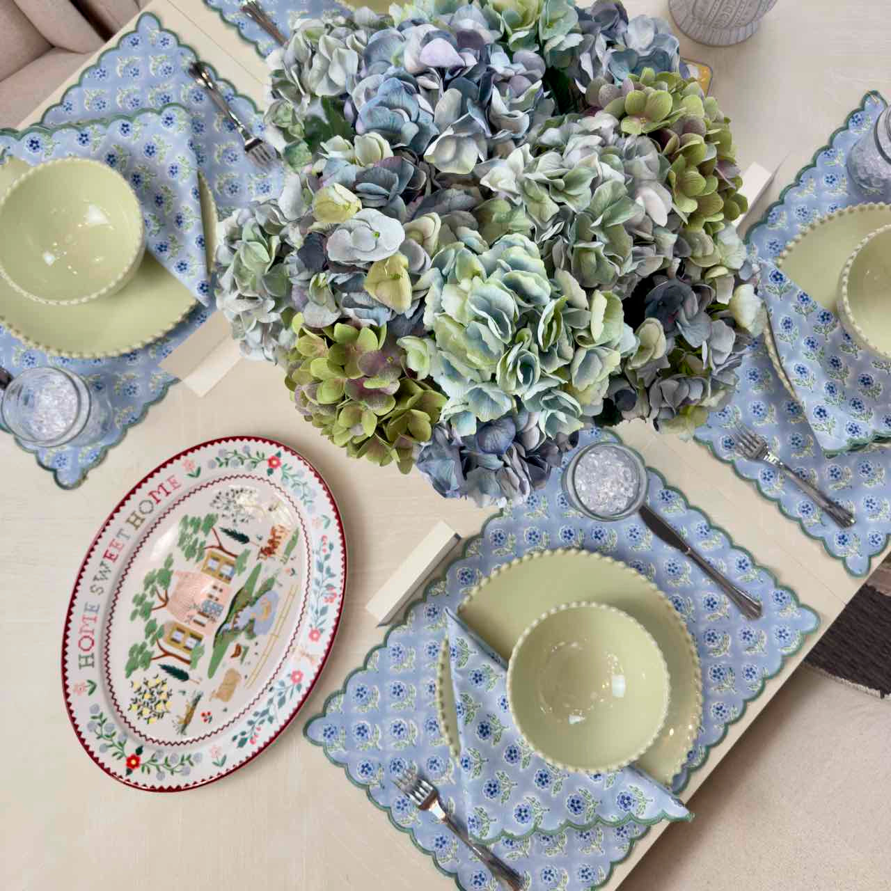 Dining table setting with floral plates, bowls, and a centerpiece of hydrangeas.