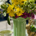Green vase with yellow and purple flowers on a blurred background