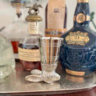 Silver shot glass on a tray with bottles of whisky in the background