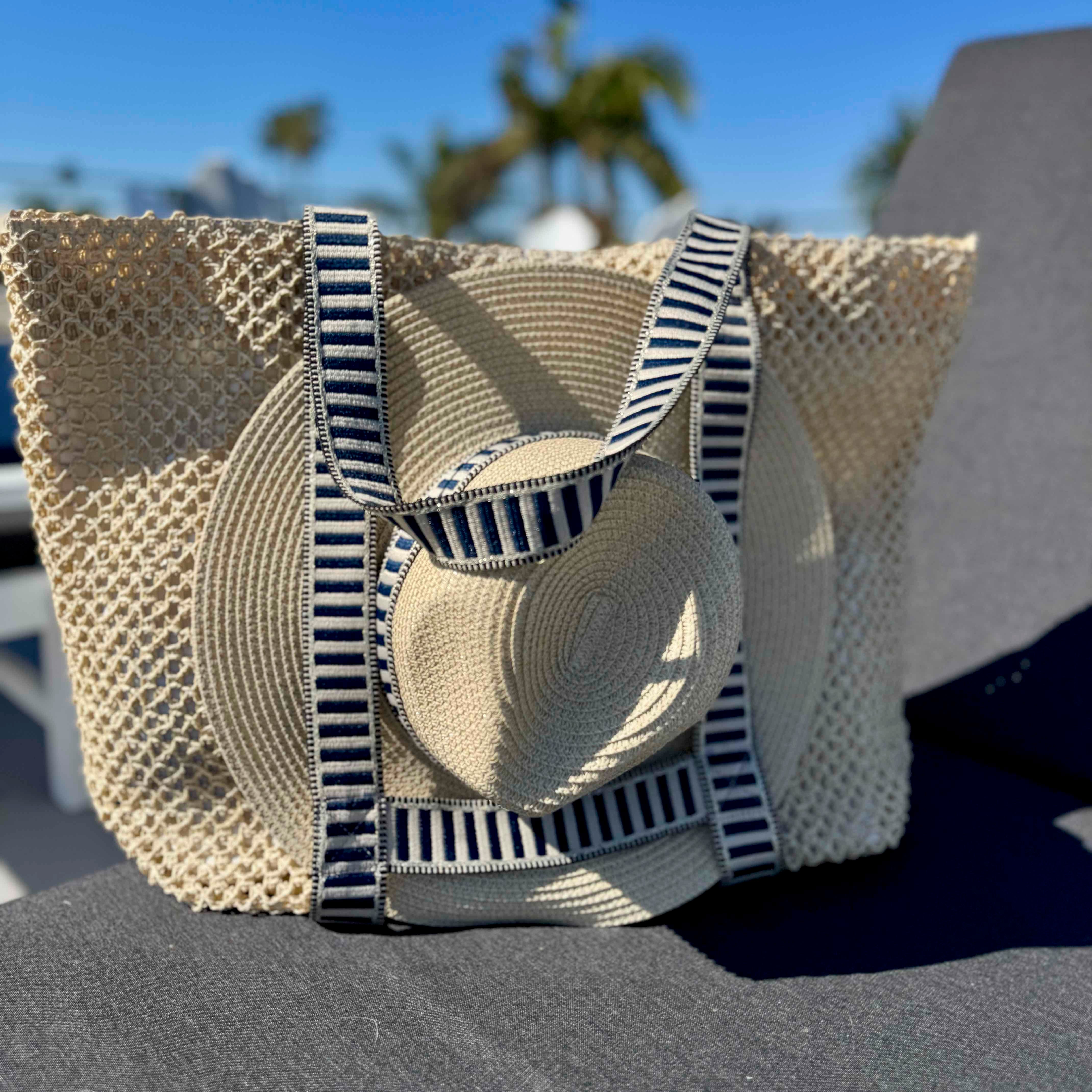 Woven straw bag with striped handles and matching sun hat on a chair outdoors.