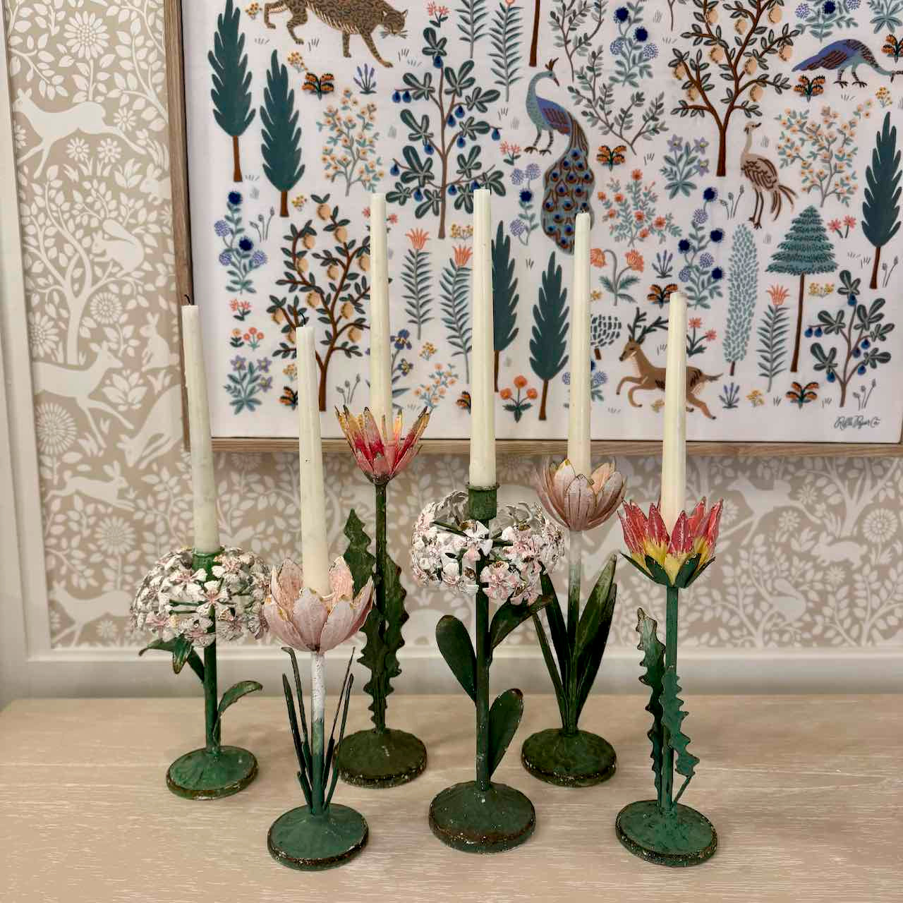 Decorative candle holders with floral designs on a wooden surface, with a patterned wall in the background.