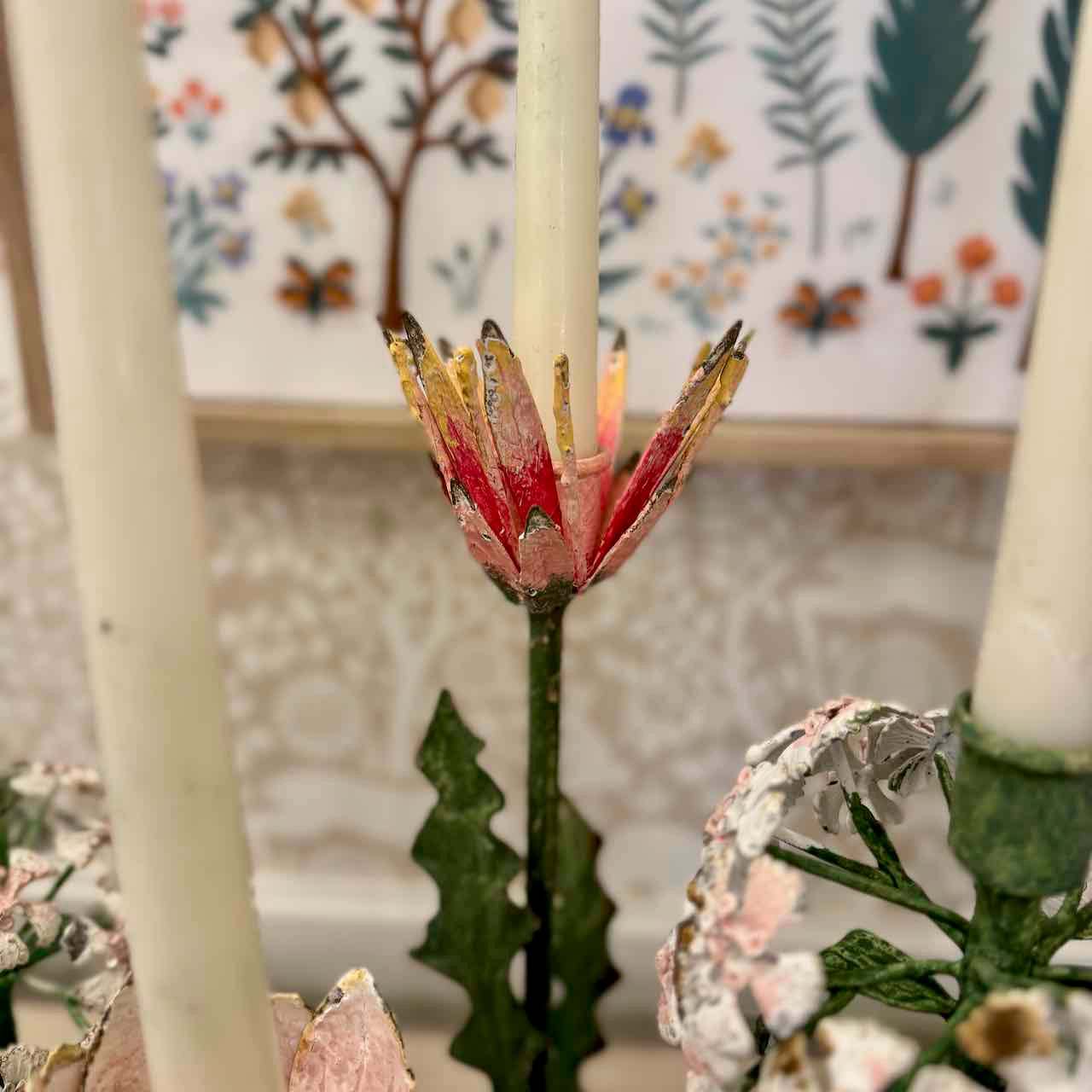 Decorative candle holder with floral design in front of a floral-patterned wall.