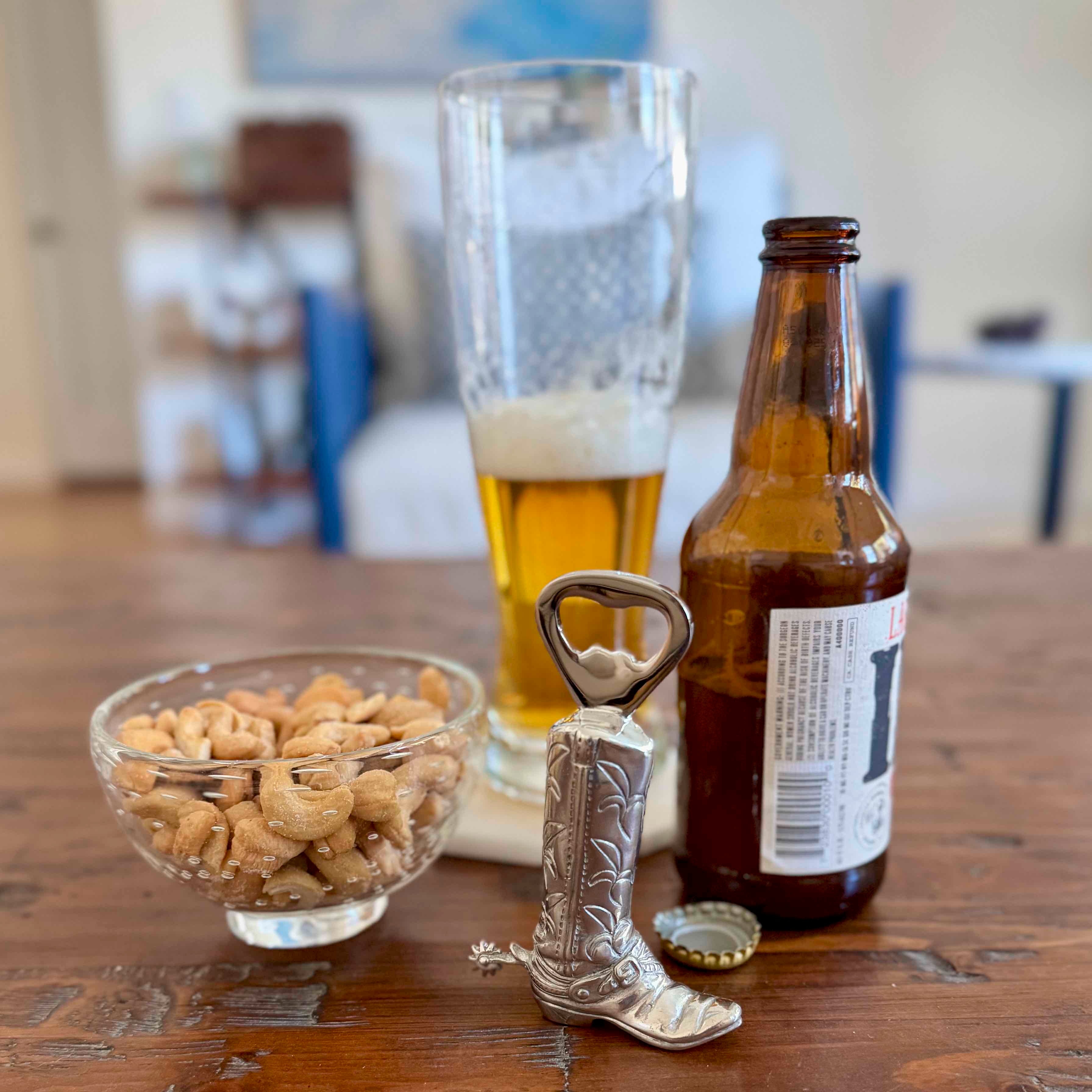 Cowboy boot bottle opener with a beer bottle, glass, and bowl of nuts on a table.