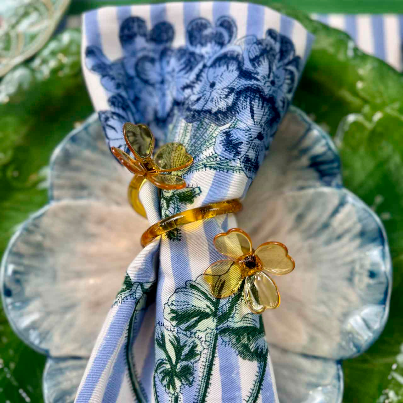 Napkin with blue floral pattern and gold flower-shaped napkin ring on a green leaf background