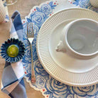 Table setting with white cup, saucer, and fork on a blue floral placemat.