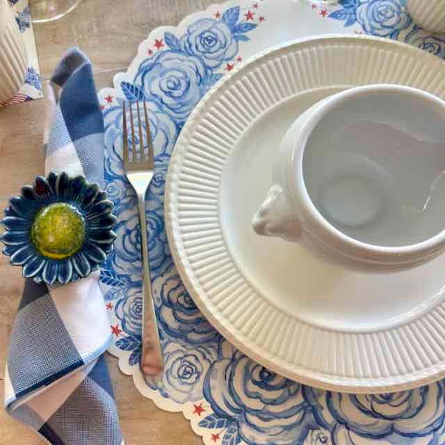 Table setting with white cup, saucer, and fork on a blue floral placemat.