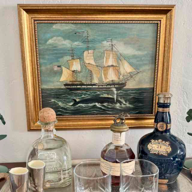 Bottles on a table with a framed painting of a ship in the background
