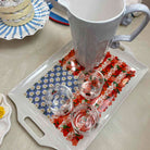 Decorative tray with floral patterns holding a white mug and small glasses on a light surface.