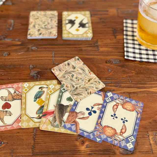 Set of decorative playing cards on a wooden surface with a glass of beer.