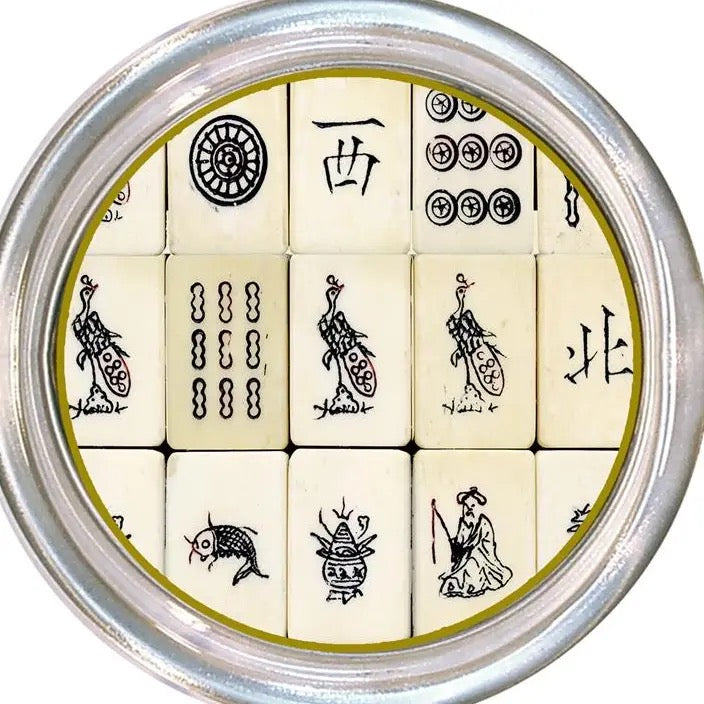 A circular silver metal tin containing 12 ivory-colored mahjong tiles with black printed symbols and characters, arranged in a 3x4 grid.