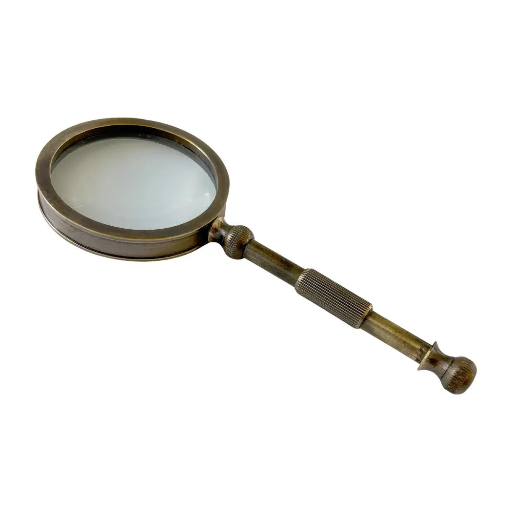 A vintage-style magnifying glass with a brass-toned metal frame and handle, featuring a knurled grip and a ribbed end, shown on a plain white background.