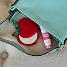 Green handbag with a red apple-shaped item and pink tube of balm on a beige surface