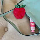 Red apple-shaped object and pink tube of 'Bestie Balm' on a beige surface