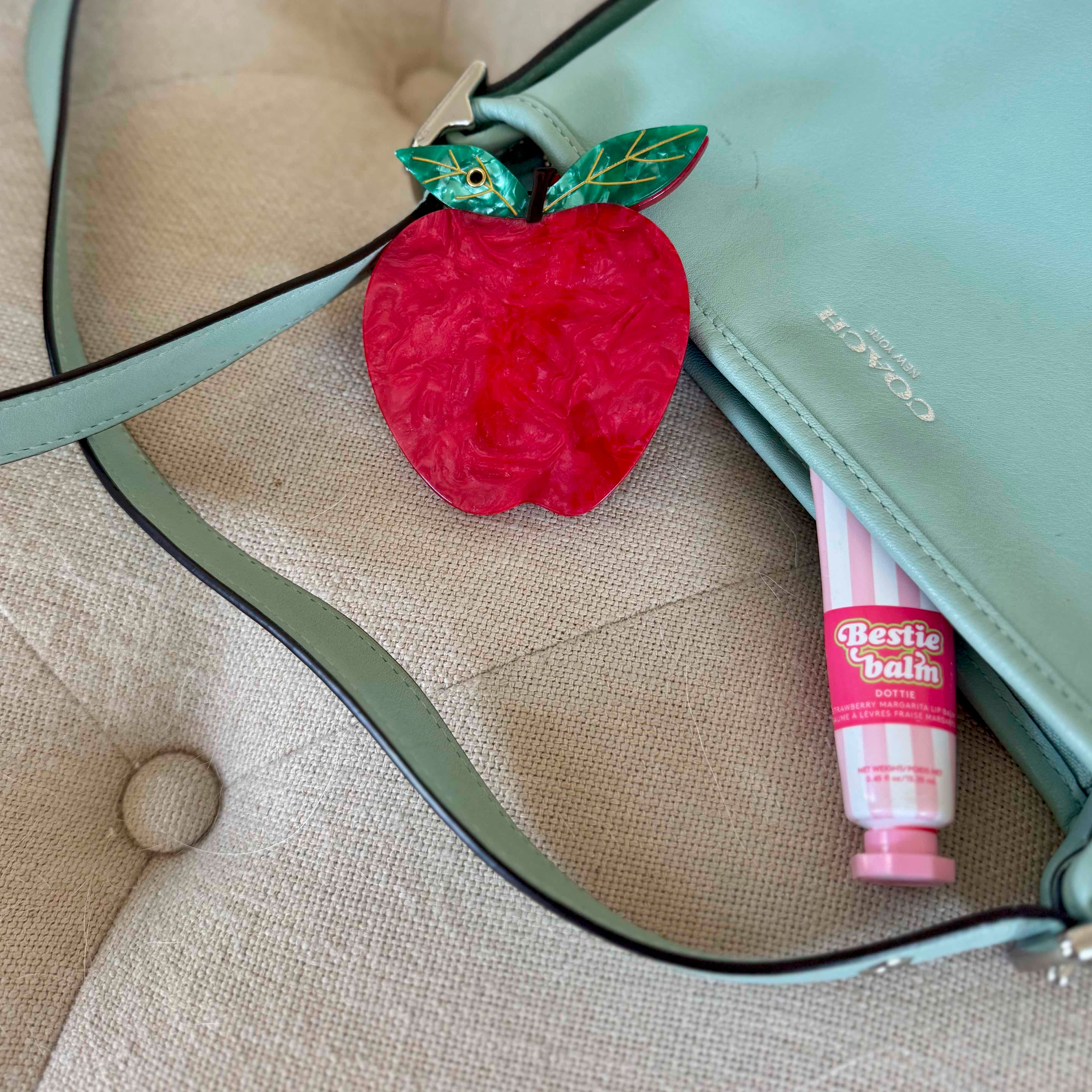 Red apple-shaped object and pink tube of 'Bestie Balm' on a beige surface