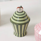 Striped ceramic jar with a decorative apple on top against a white background
