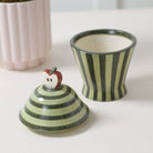 Ceramic container with striped design and apple-shaped knob on a white surface