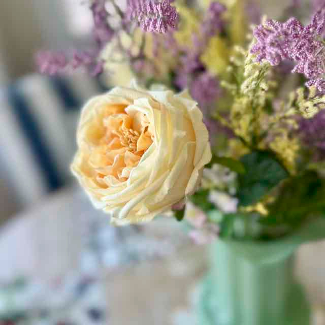 Bouquet of flowers with a prominent white rose in a green vase.