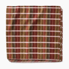 Folded fabric with a plaid pattern featuring brown, red, and beige colors on a white background.