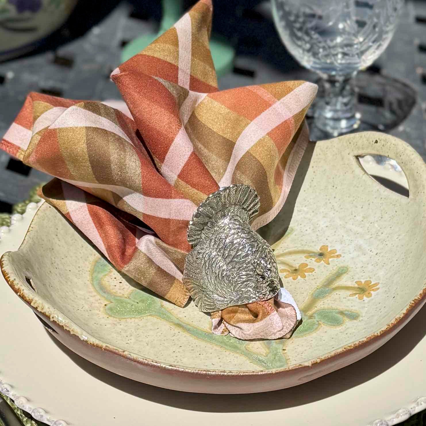 Decorative plate with a floral design, a silver napkin holder, and a patterned napkin on a table setting.