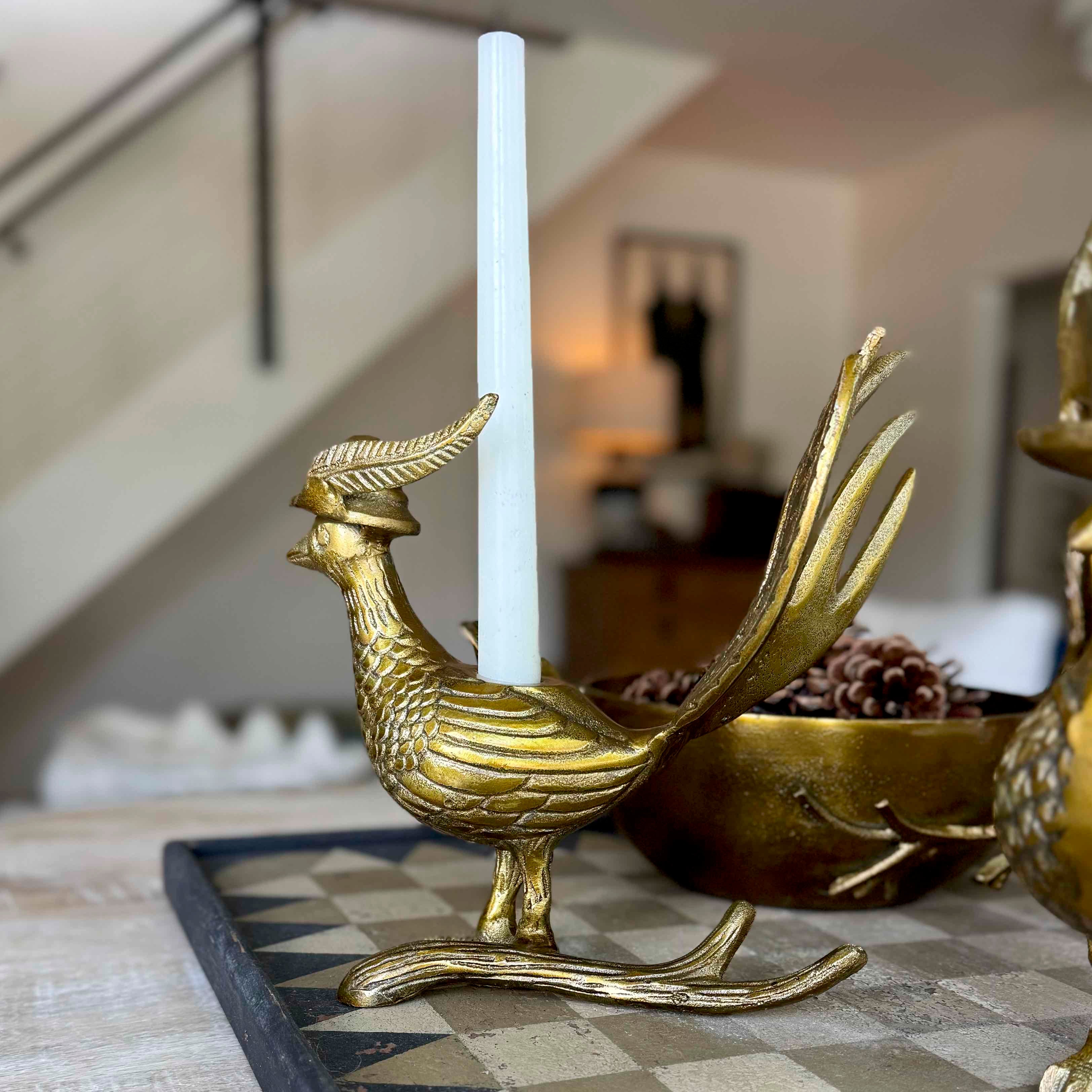 Gold rooster candle holder with a white candle on a checkered surface