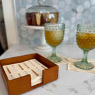 Wooden coaster set with business cards on a marble surface, with two glasses of a yellowish beverage in the background.
