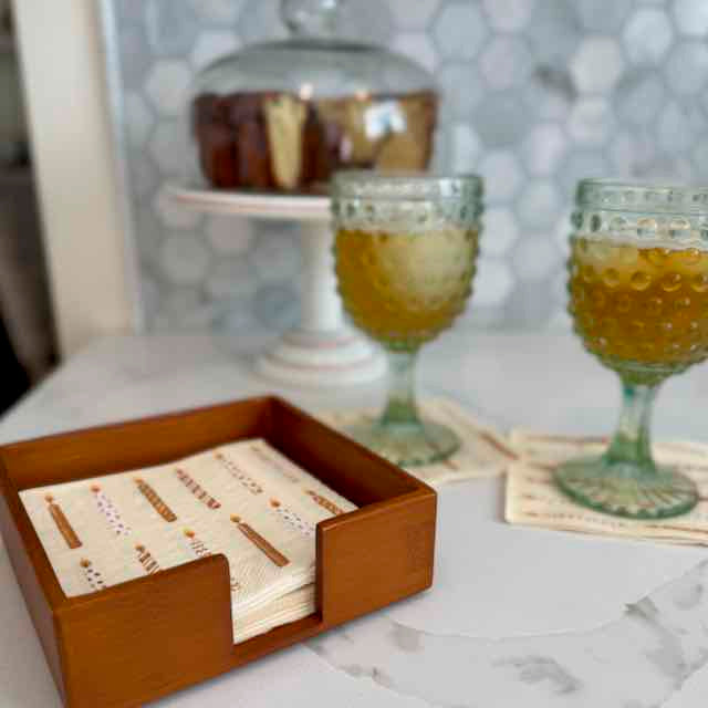 Wooden coaster set with business cards on a marble surface, with two glasses of a yellowish beverage in the background.
