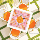 Decorative placemat with a pink design on a table surrounded by orange chairs.