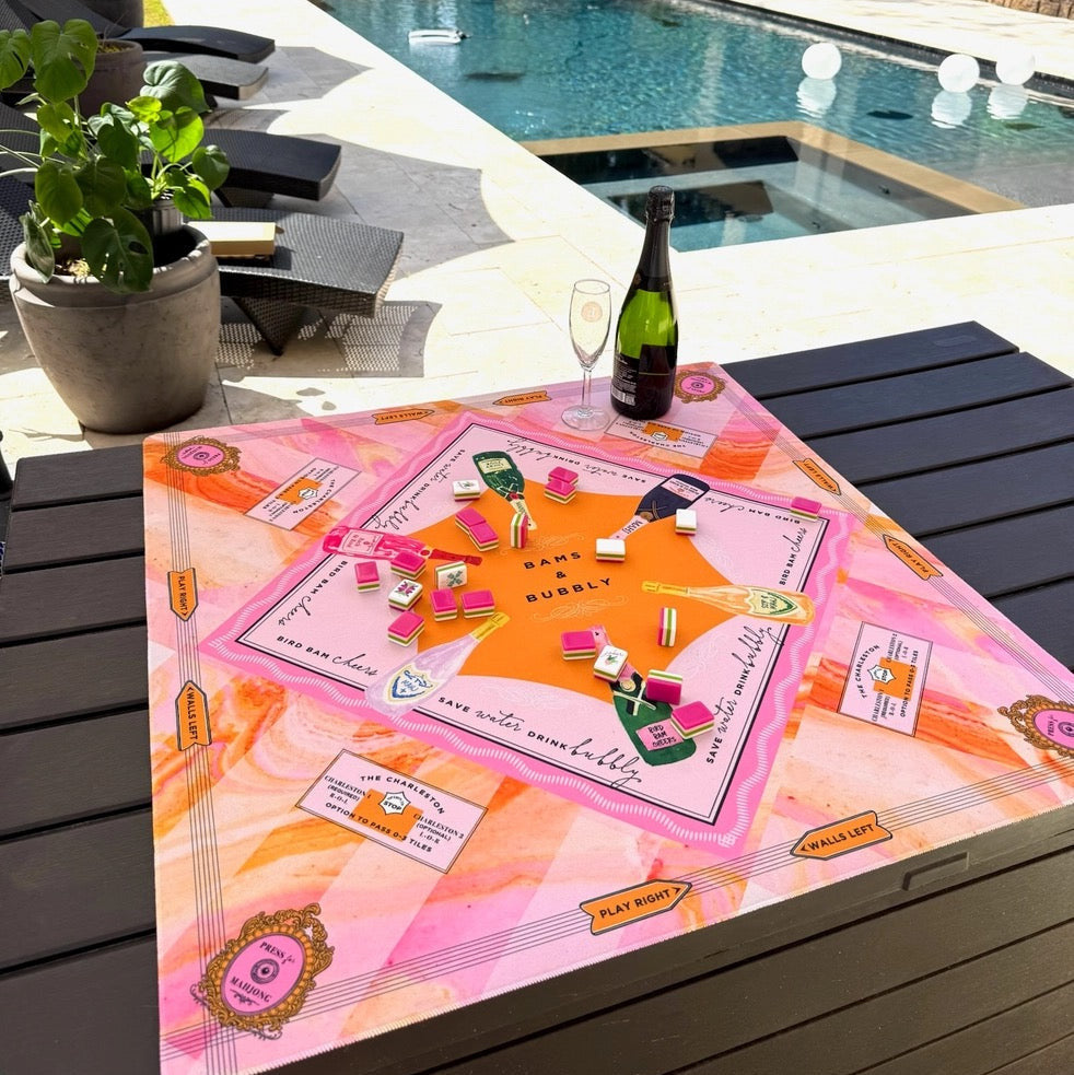 Board game on a table by a poolside with a bottle of champagne.