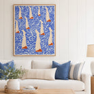 A framed abstract art print featuring stylized sailboats on a blue wavy background, displayed on a white paneled wall above a white sofa with blue and striped pillows.