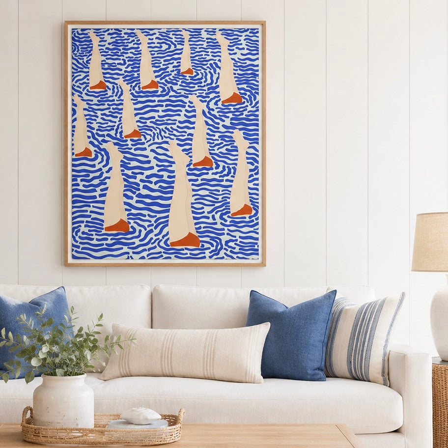 A framed abstract art print featuring stylized sailboats on a blue wavy background, displayed on a white paneled wall above a white sofa with blue and striped pillows.