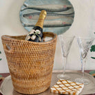 Wicker wine cooler with bottle of champagne, two glasses, and a decorative plate on a table.
