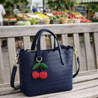 Navy blue handbag with cherry embellishments on a wooden bench at an outdoor market.