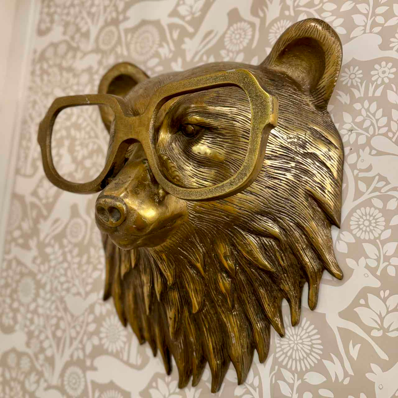 Bronze bear head sculpture wearing glasses on a decorative wall background