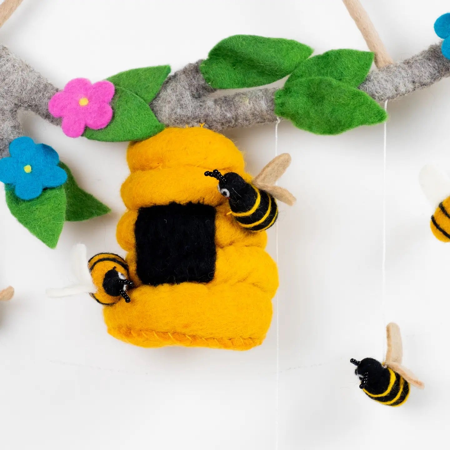 Toy bee hive with bees and flowers on a branch against a white background