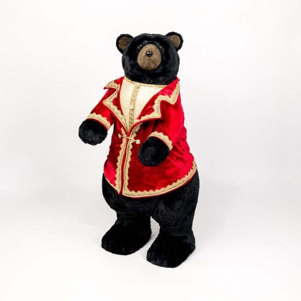 Black teddy bear wearing a red velvet jacket with gold trim on a white background