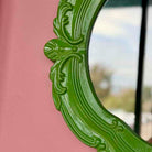 Decorative green mirror with intricate patterns on a pink wall
