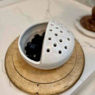 White ceramic tea ball with black tea leaves on a wooden coaster.