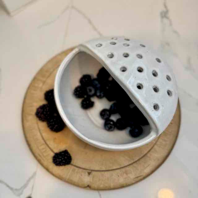 White ceramic colander with blackberries on a wooden board