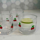 Three clear glasses with cherry designs on a white surface.